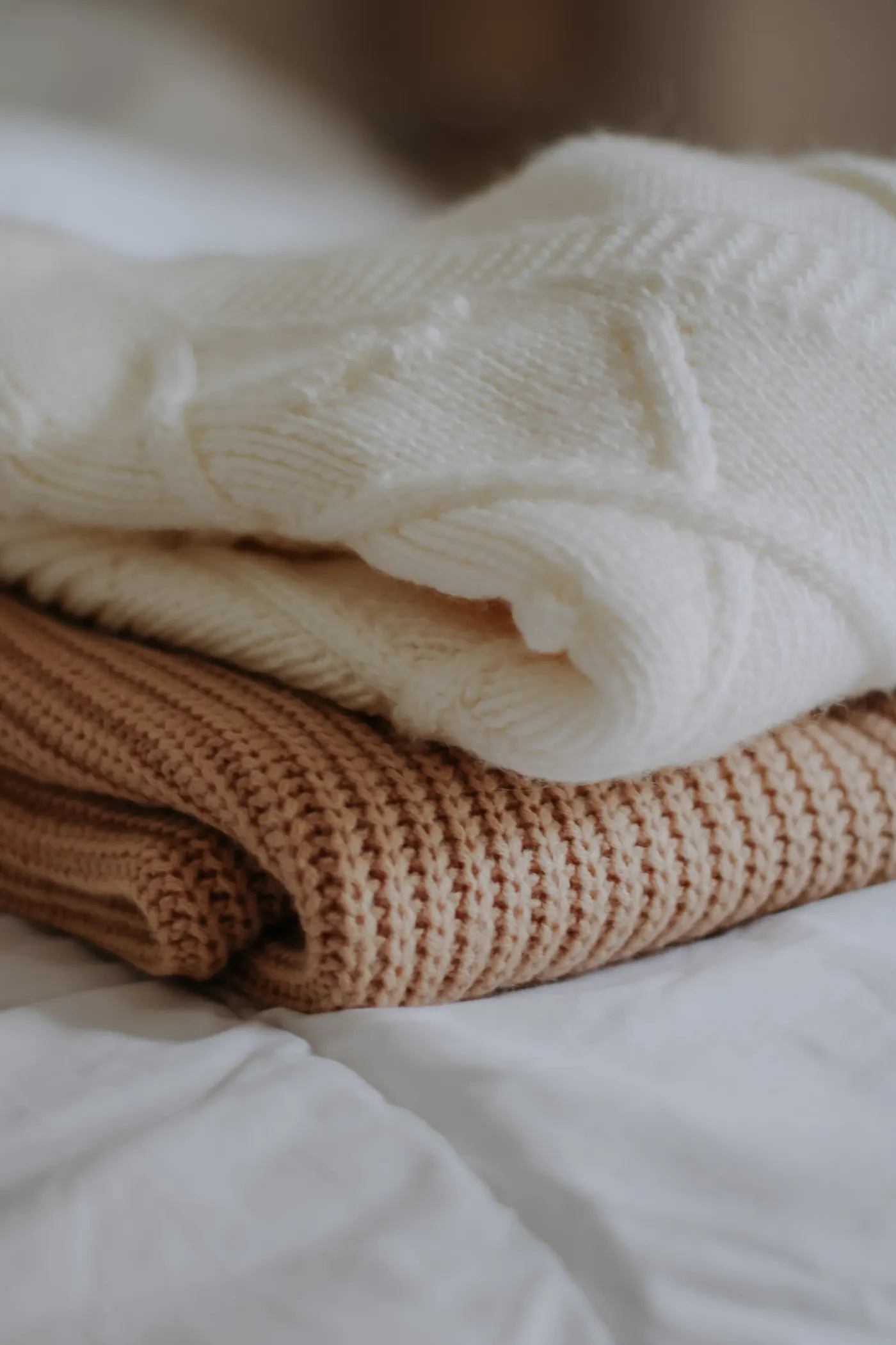 Wool sweaters stacked on bedding